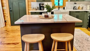 Una cocina con una isla central, taburetes de madera y armarios verdes.