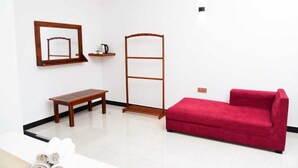 Ein Zimmer mit einem roten Sofa, einer Holzbank, einem Wäscheständer aus Metall, einem kleinen Tisch mit Wasserkocher und einem Spiegel an der Wand.