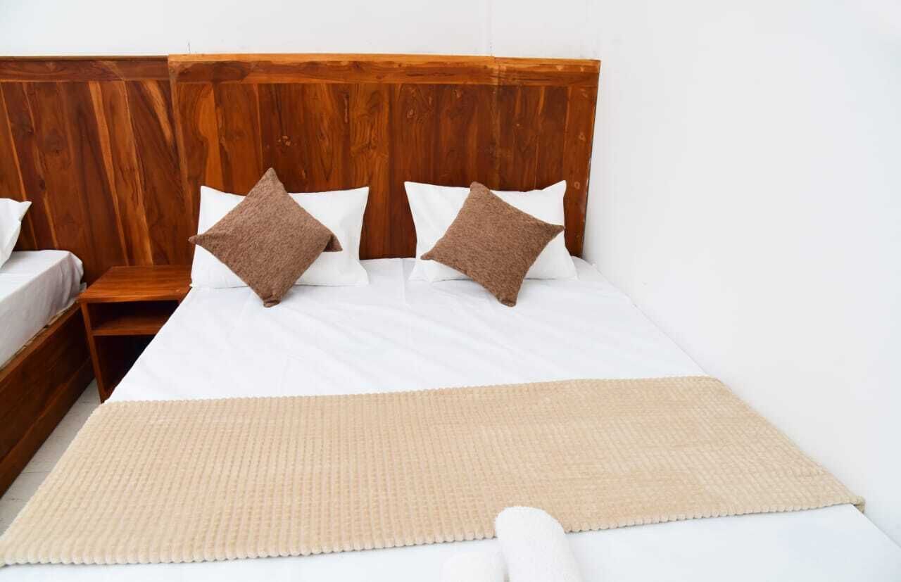 A bed with a wooden headboard, two pillows, a white mattress, and a beige blanket.