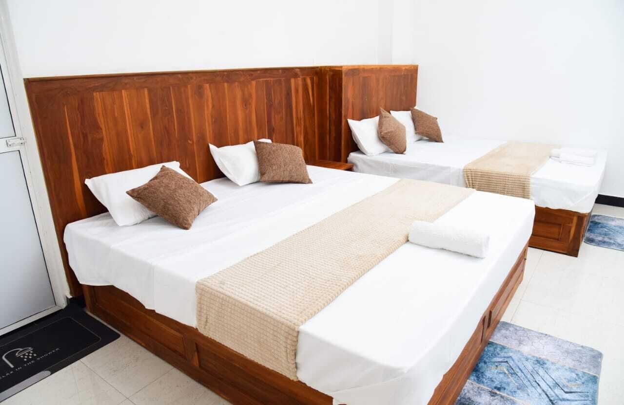 A hotel room with two beds, wooden headboards, white linens, and brown throw pillows.