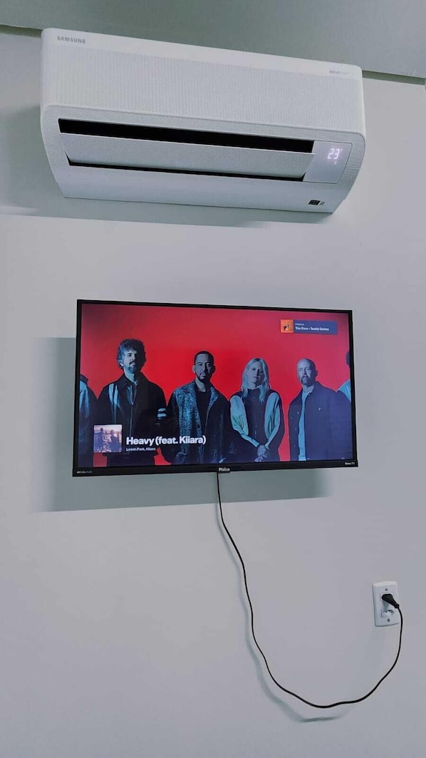 Un aire acondicionado de pared y un televisor mostrando un video musical.