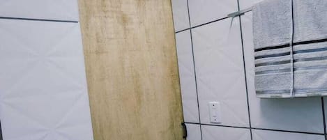 A bathroom with white tiled walls, a wooden door, and a towel hanging on the wall.