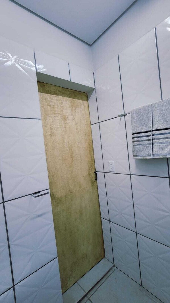 A bathroom with white tiled walls, a wooden door, and a towel hanging on the wall. - Suítes Caminho do Pantanal  (Aquidauana)