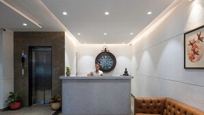 A reception area with a marble reception desk, a clock, a sofa, and an elevator. - StayBird - Azure Suites Business Hotel (Pune)