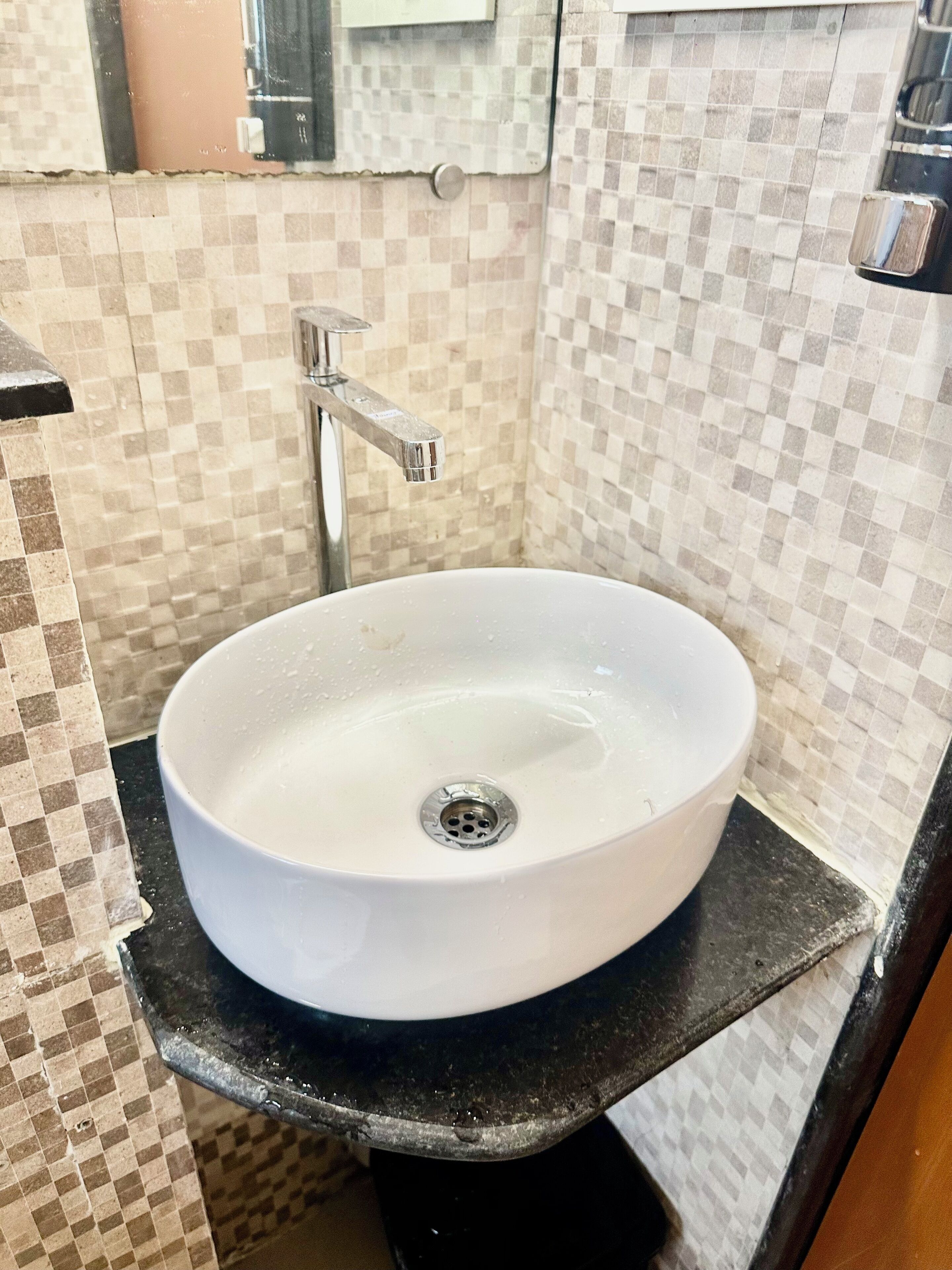Une salle de bain avec un lavabo blanc, un plan de toilette noir et un mur recouvert de carreaux disposés en motif à carreaux.