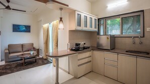 A modern kitchen with a built-in stove, a refrigerator, and a window. There is a dining area with a sofa and a coffee table. - StayBird - Azure Suites Business Hotel (Pune)