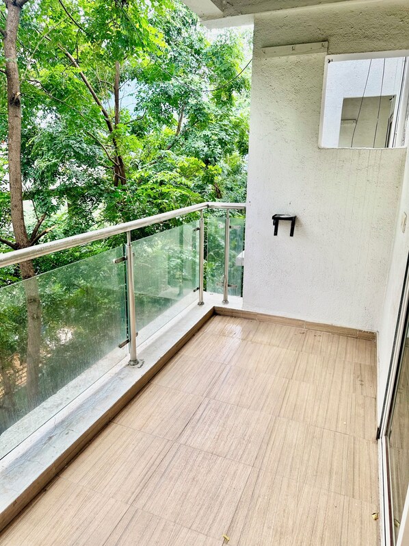 A balcony with a glass railing, a small table, and a view of trees. - StayBird - Azure Suites Business Hotel (Pune)