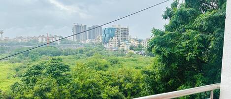 A balcony with a metal railing overlooking a lush green landscape and a cityscape in the distance.