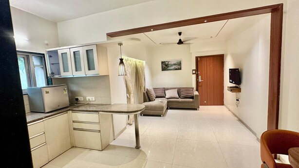 A modern kitchen with white cabinets, a built-in oven, and a dining area with a round table. - StayBird - Azure Suites Business Hotel (Pune)