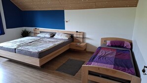 A bedroom with a large bed, a smaller bed, a nightstand, and a wall-mounted shelf. - Large, cozy and family-friendly vacation apartment with balcony and garden (Bischbrunn)