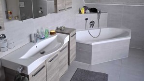 A modern bathroom with a freestanding bathtub, a large mirror, and a vanity with a sink and storage. - Large, cozy and family-friendly vacation apartment with balcony and garden (Bischbrunn)