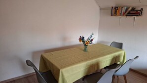 A dining area with a table covered in a yellow tablecloth, surrounded by four chairs. A vase with flowers is placed on the table. - Large, cozy and family-friendly vacation apartment with balcony and garden (Bischbrunn)