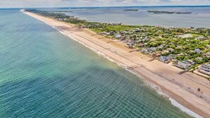 Vue aérienne d’une ville côtière avec une longue plage de sable, des quartiers résidentiels et un port de plaisance.