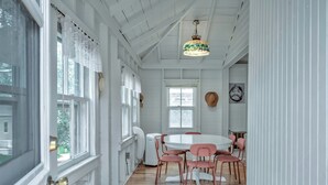 Un coin repas avec une table ronde et des chaises roses, des murs blancs et un plafond en bois.