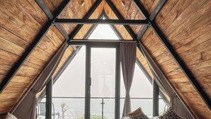 Een gezellig zolderkamer met twee bedden, houten balken en een groot raam met uitzicht op het omliggende landschap.