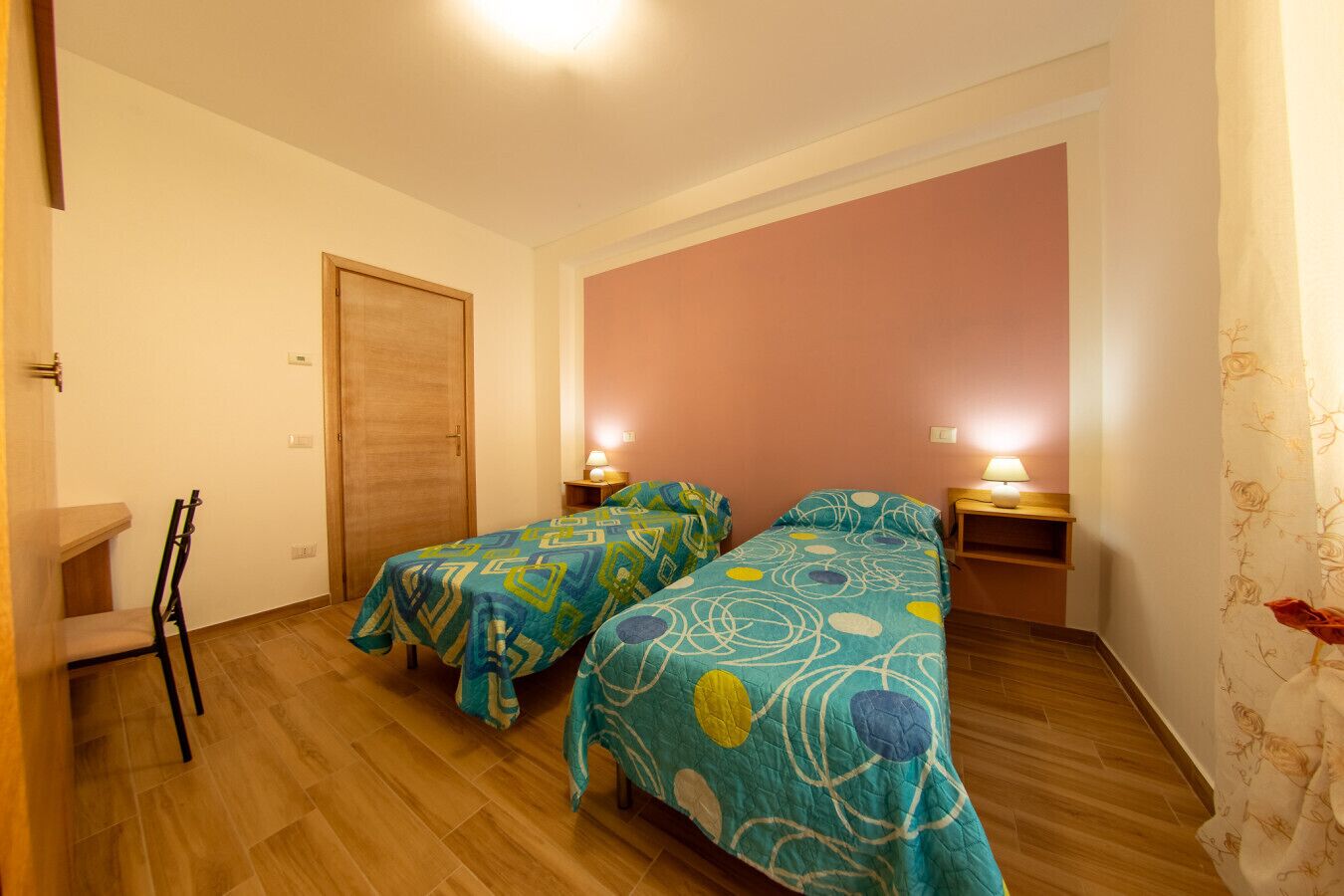 A room with two beds, wooden floors, a door, and a chair.