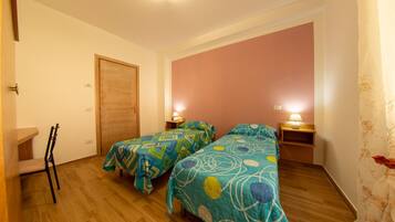 A room with two beds, wooden floors, a door, and a chair.
