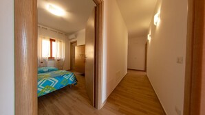 Ein schmaler Flur mit Holzboden, einem Bett mit bunter Bettdecke und einer Tür zu einem weiteren Raum.