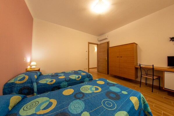 A bedroom with two beds, a desk, a chair, and a wardrobe.