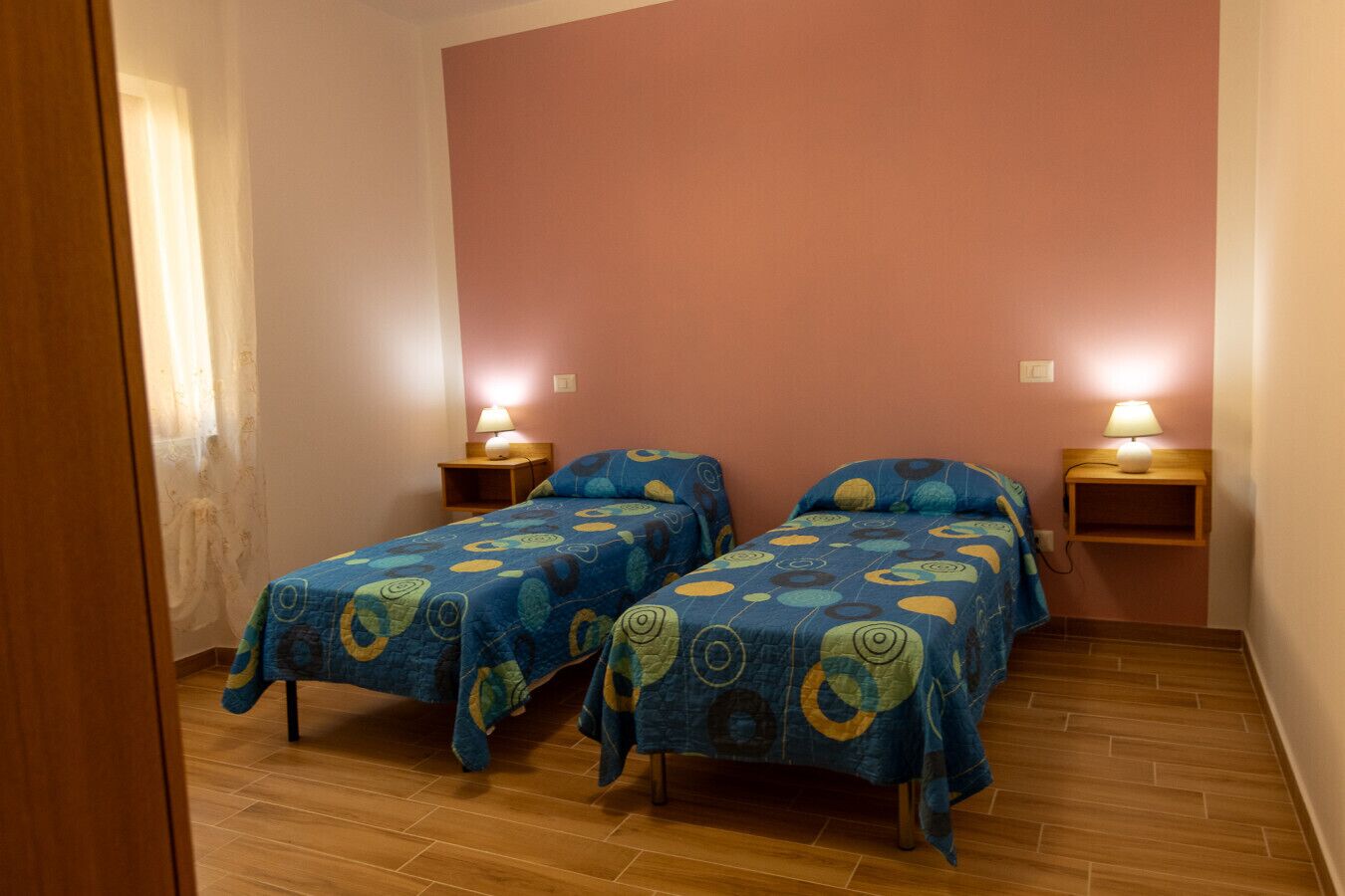 Une chambre avec deux lits, chacun recouvert d’une couvre-lit à motifs, des tables de chevet en bois avec des lampes, et un plancher en bois.