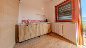 Une petite cuisine avec des meubles en bois, un pare-feu en carreaux et une fenêtre avec des stores.