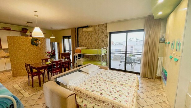 Ein Hotelzimmer mit Bett, Esstisch, Stühlen, einer kleinen Küche und einem Balkon mit Blick.