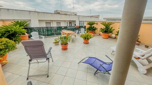Eine Dachterrasse mit Topfpflanzen, Gartenmöbeln und freiem Blick auf die umliegenden Gebäude.