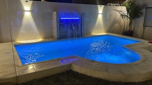 Una piscina con una cascada y un muro de piedra.