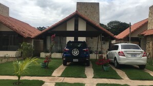 Una casa con garaje, dos coches aparcados en la entrada y un césped bien cuidado con macetas.