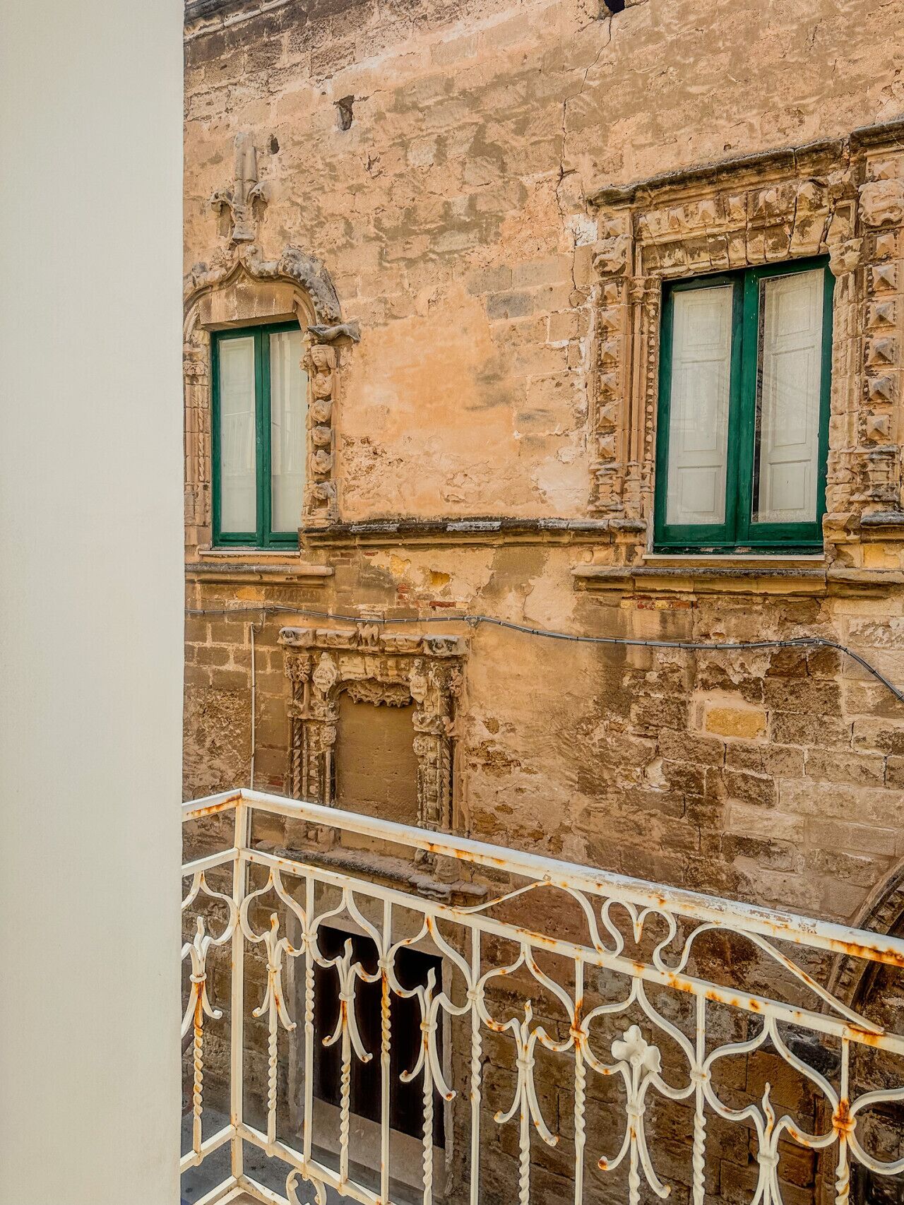 A weathered building facade with two windows, each with green shutters and decorative stonework.