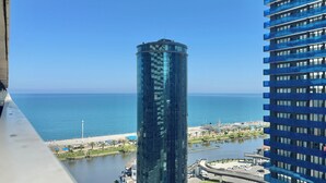 Ein Hochhaus mit Glasfassade blickt auf ein Ufergebiet mit Strand und einem Wasserlauf.