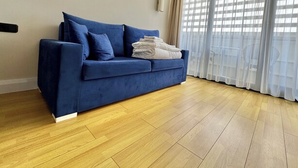 Ein Zimmer mit einem blauen Sofa, einer weißen Klimaanlage und einem großen Fenster mit durchsichtigen Vorhängen.
