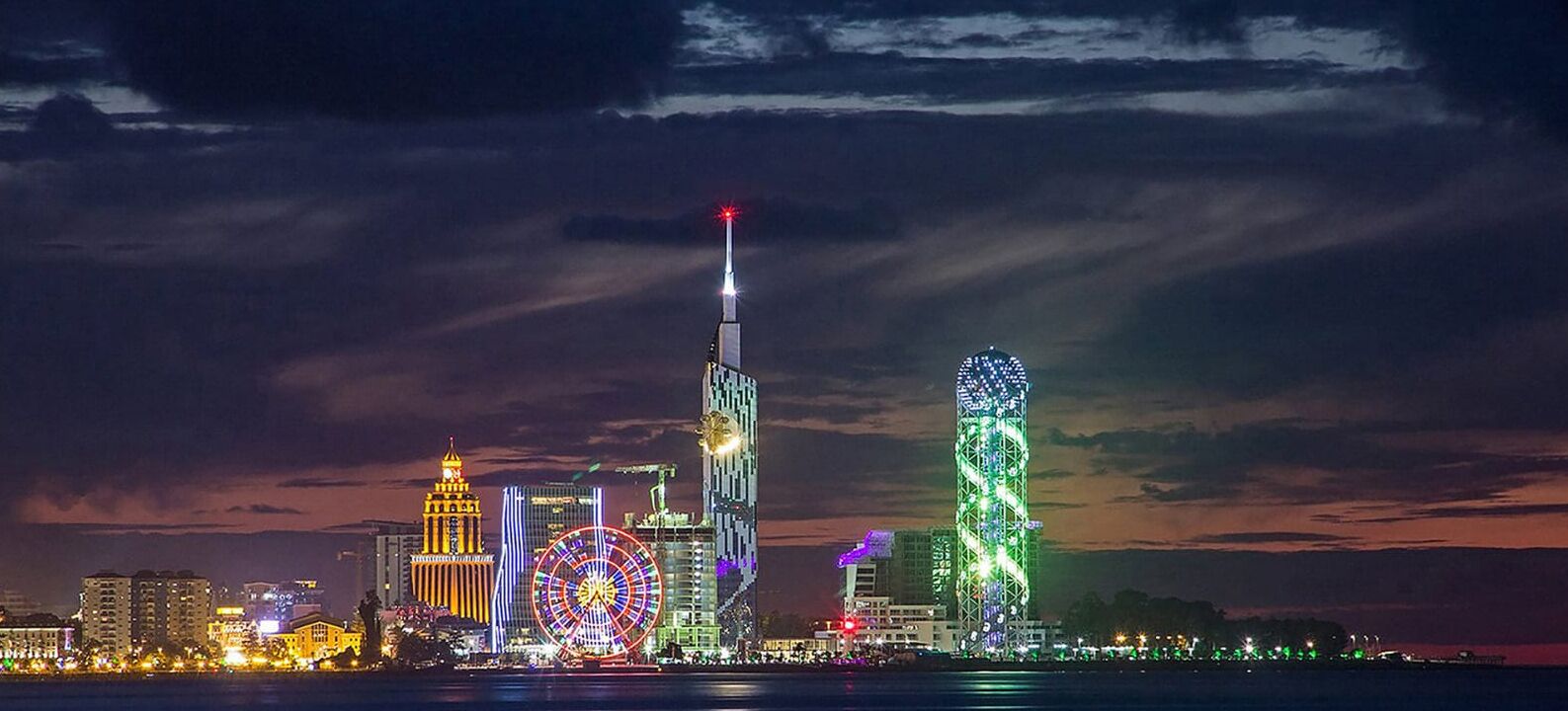 Silhueta urbana noturna com edifícios iluminados e uma roda gigante.