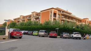 Un estacionamiento con varios coches aparcados frente a un edificio de varios pisos con balcones.