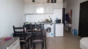 Cocina compacta con lavadora, microondas y comedor con sillas y mesa.