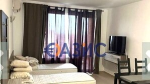 Una habitación pequeña y bien iluminada con una cama individual, un televisor, un escritorio y una silla.