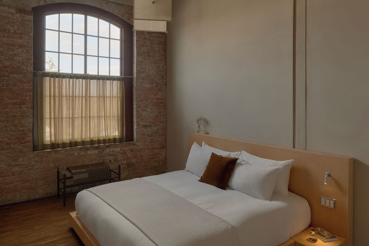 A bedroom with a large window, a bed, a bedside table, and a bench.