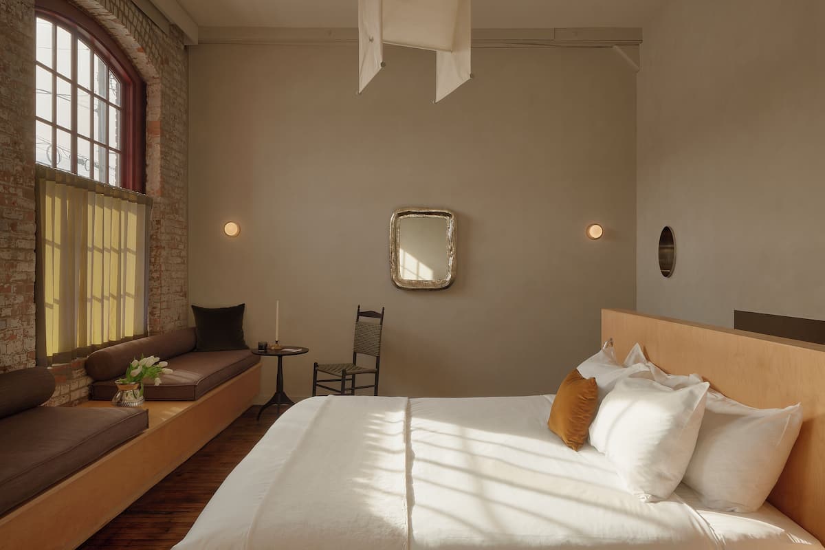 A bedroom with a bed, a seating area with a chair, a small table, and a window with a view.