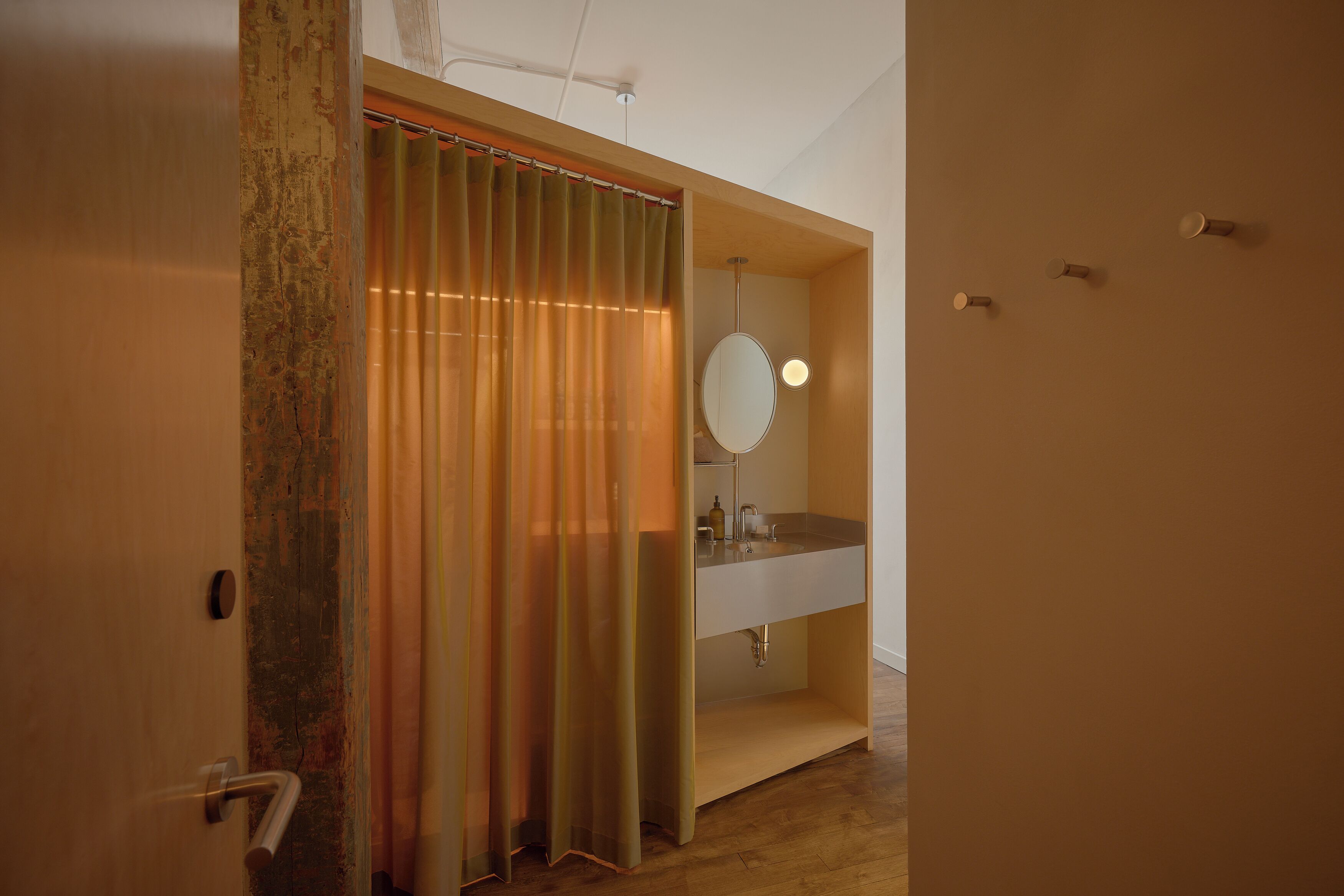 Un baño con puerta de madera, cortina de ducha, espejo y lavamanos.