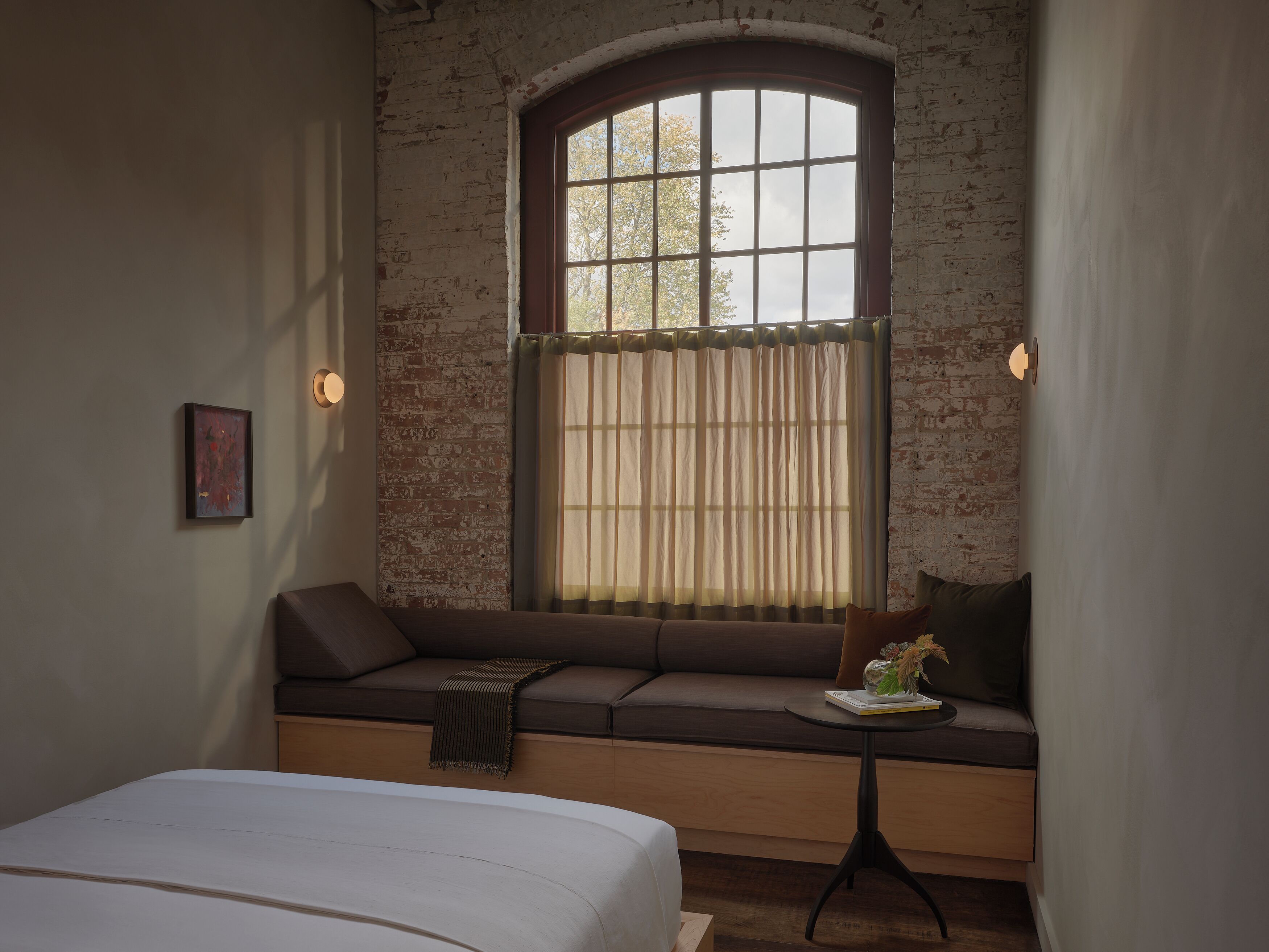 A room with a large window, a sofa, a small table, and a bed.