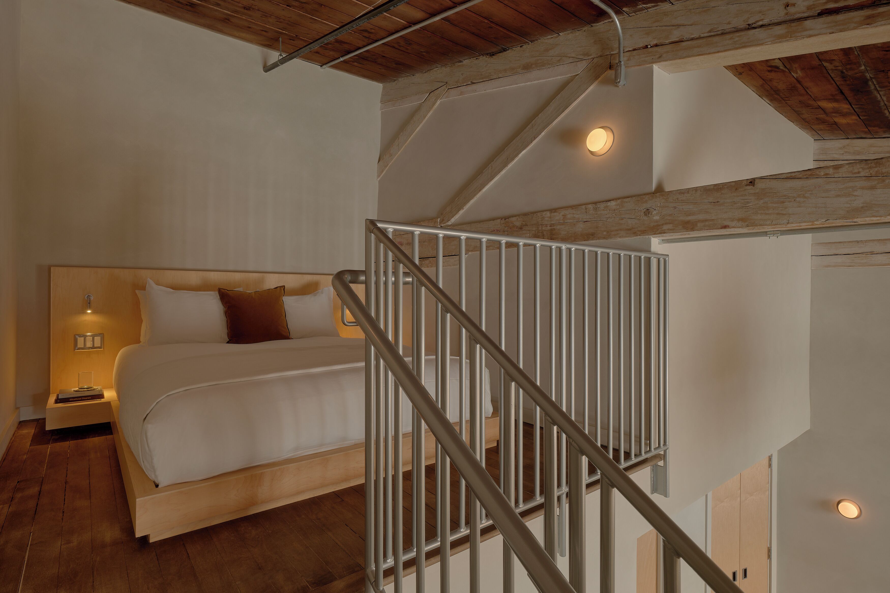 Quarto com cama, mesa de cabeceira e escada com corrimão.