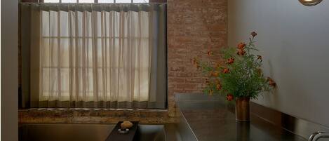 Una cocina moderna con una ventana, un lavamanos, un florero con flores y una lámpara redonda.