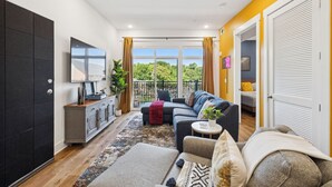 A modern living room with a sofa, a TV, a plant, and a balcony with curtains.