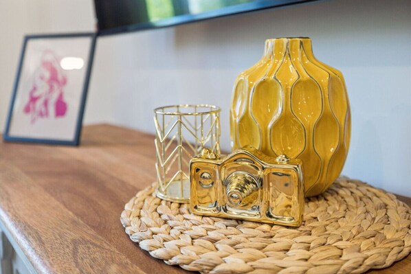 A wooden table with a woven placemat, a yellow vase, and a decorative glass object.
