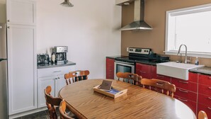 Uma cozinha compacta com uma mesa de jantar, cadeiras de madeira, cafeteira e fogão.