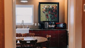 Uma cozinha compacta com área de refeições, com pia, cafeteira, micro-ondas e um quadro floral emoldurado.