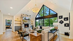 A spacious living room with a fireplace, large windows, and a modern chandelier. - Lakefront Lake Anna, Beach, Dock, Deck Vie (Bumpass)
