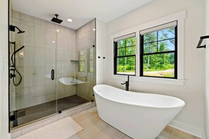 Ein modernes Badezimmer mit einer freistehenden Badewanne, einer Duschkabine und einem Fenster mit Blick auf Grünflächen.
