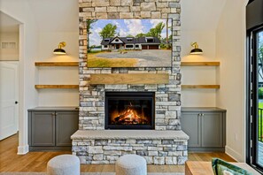 A stone fireplace with a television above it, flanked by grey cabinets and two wooden shelves.