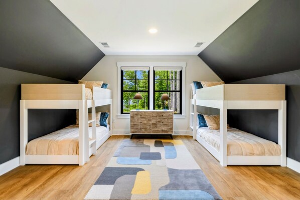A room with two bunk beds, a wooden dresser, and a large window with a view of trees.